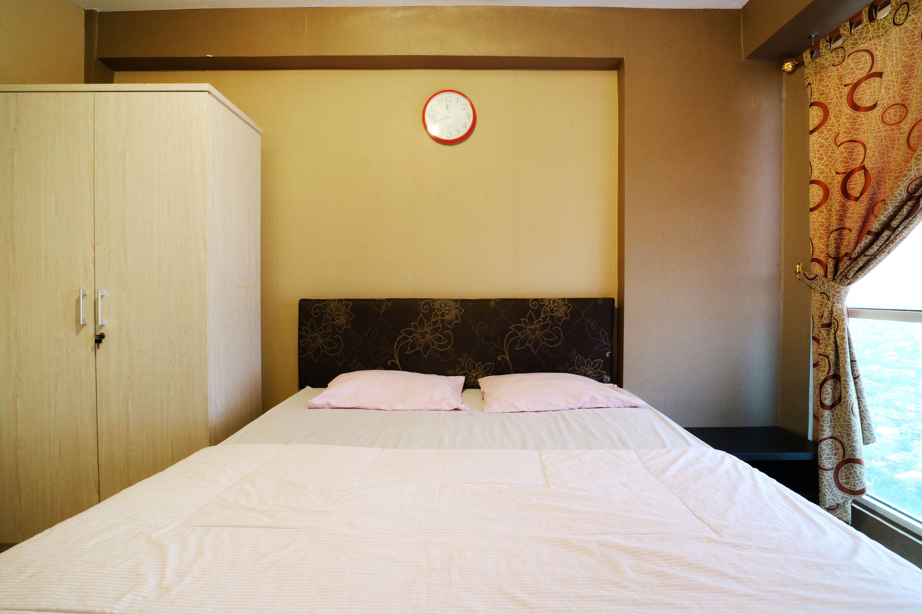 Une chambre d’hôtel avec un lit, une armoire, une horloge au mur et une fenêtre avec des rideaux.