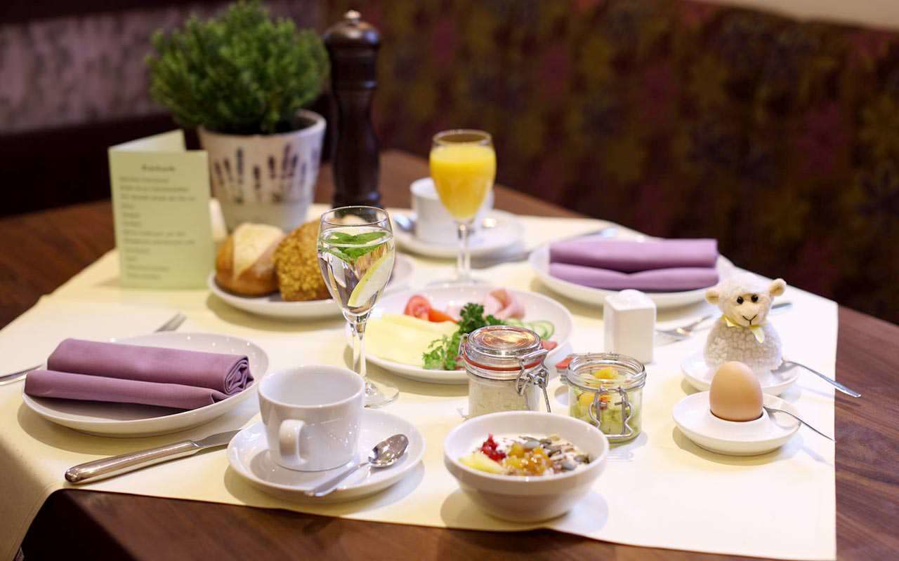 Desayuno servido con platos de comida, un vaso de jugo de naranja y una pequeña figura decorativa de un pájaro.
