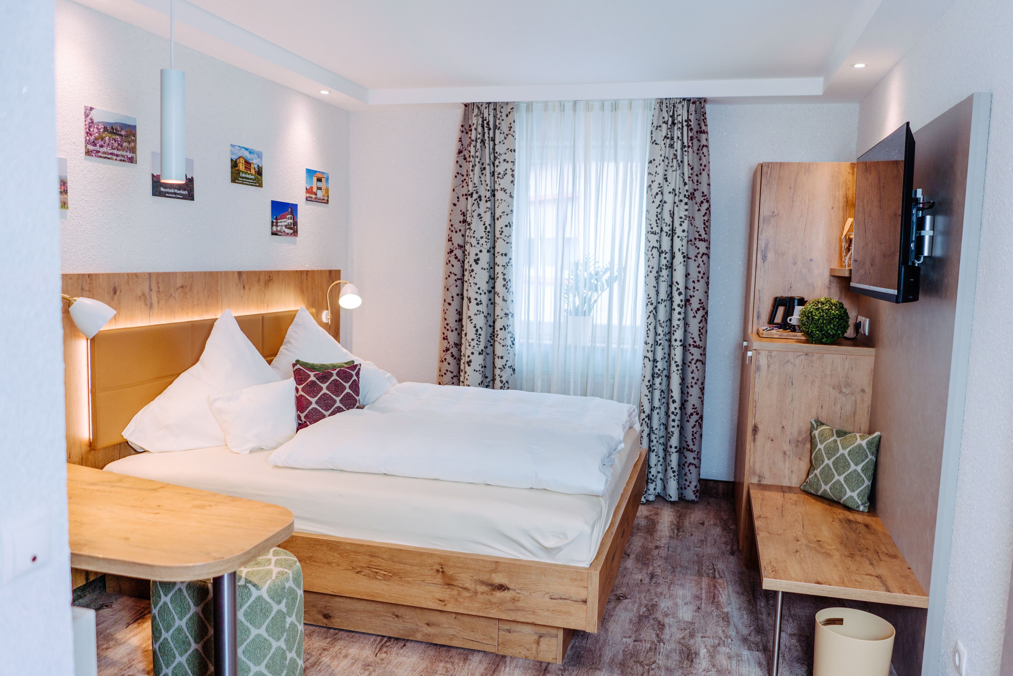 Une chambre d’hôtel moderne avec un lit en bois, un petit bureau, une télévision et une fenêtre avec des rideaux.