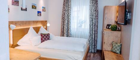 A modern hotel room with a wooden bed, a small desk, a TV, and a window with curtains.