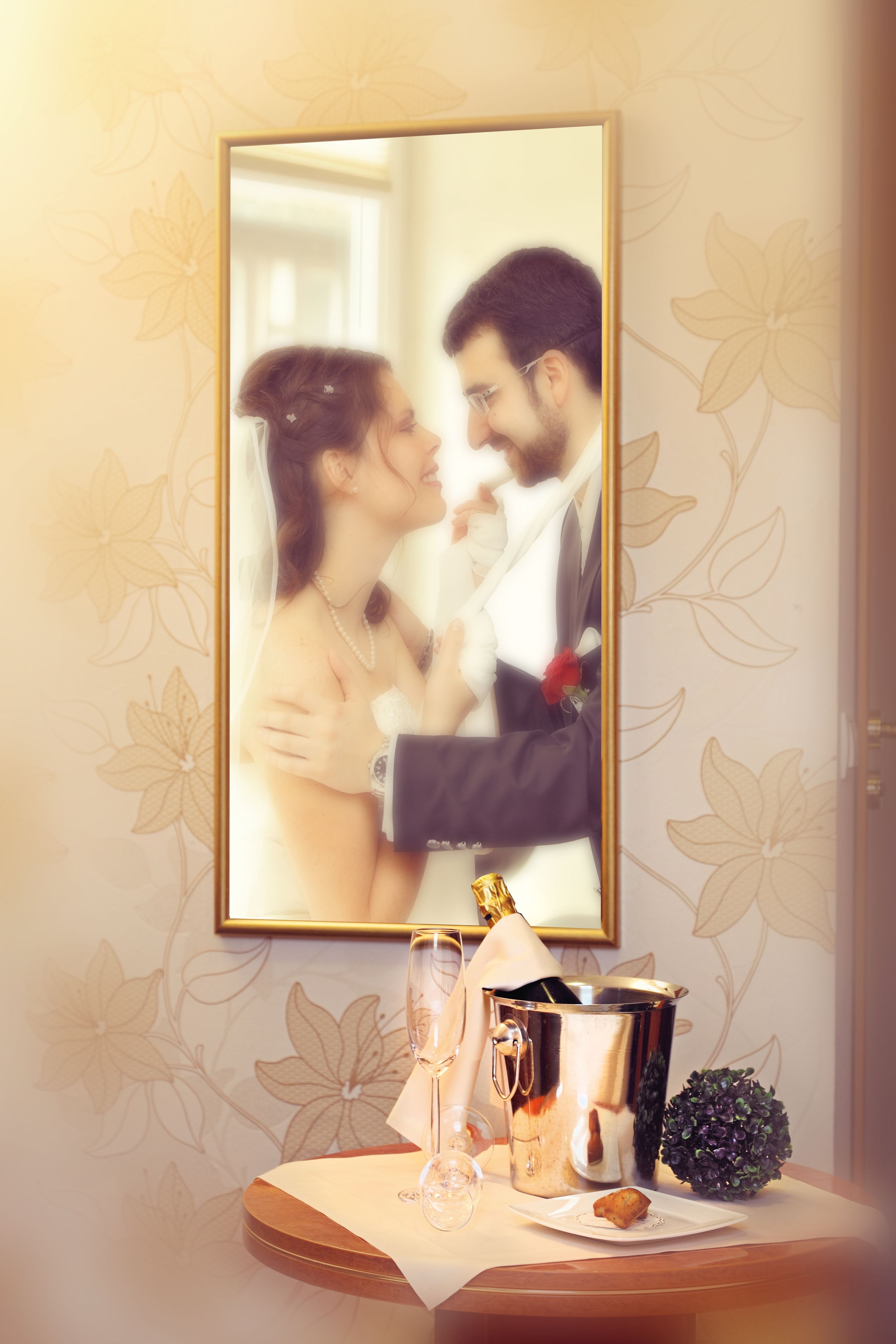 Une photographie encadrée représentant un couple, une coupe à champagne, une bouteille et un objet décoratif posés sur une table.
