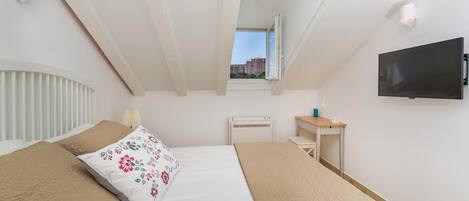Ein Schlafzimmer mit Bett, Schreibtisch, Fernseher und einem Fenster mit Blick auf Gebäude.