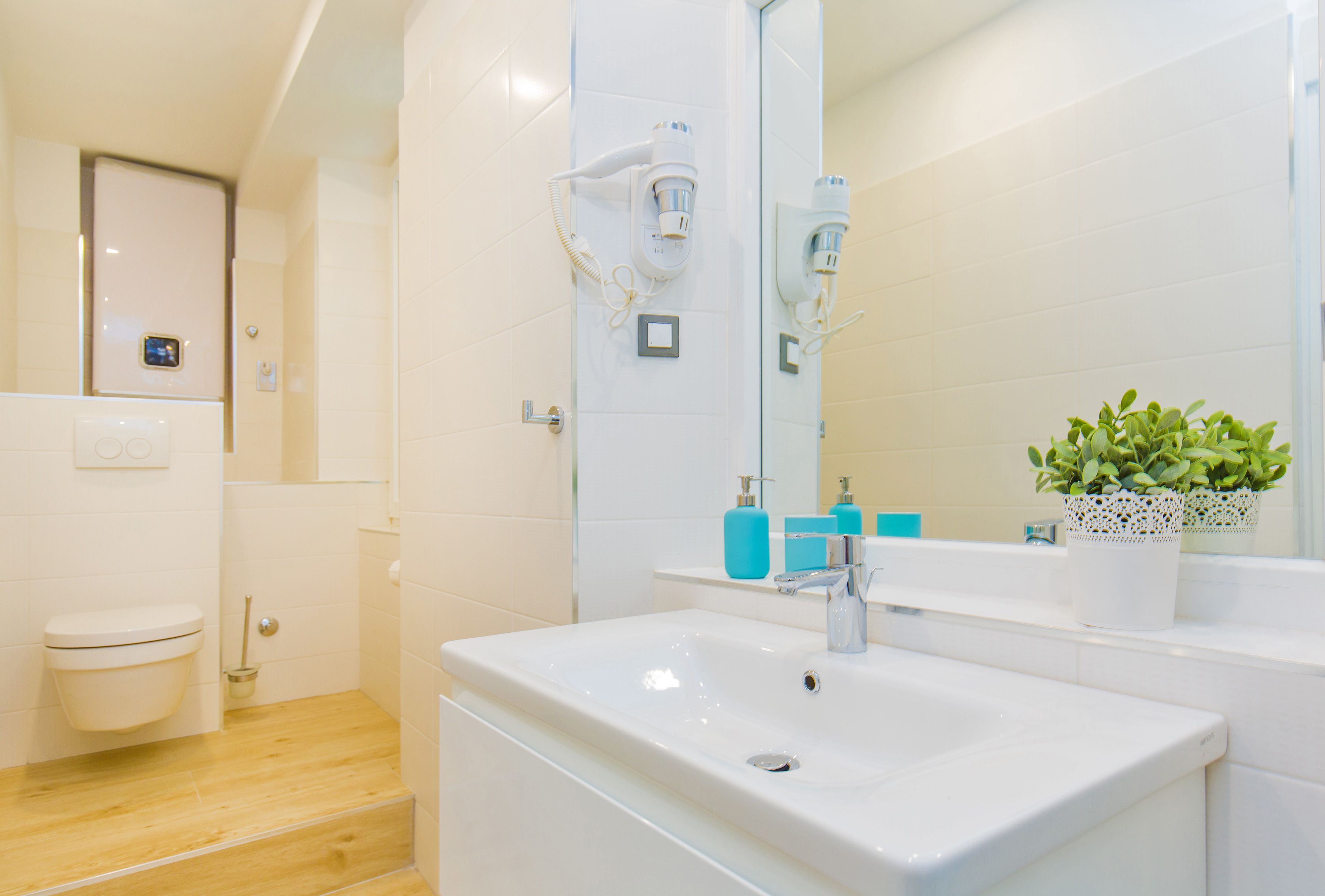 Een moderne badkamer met een witte wastafel, een spiegel en een aan de muur bevestigde haardroger.