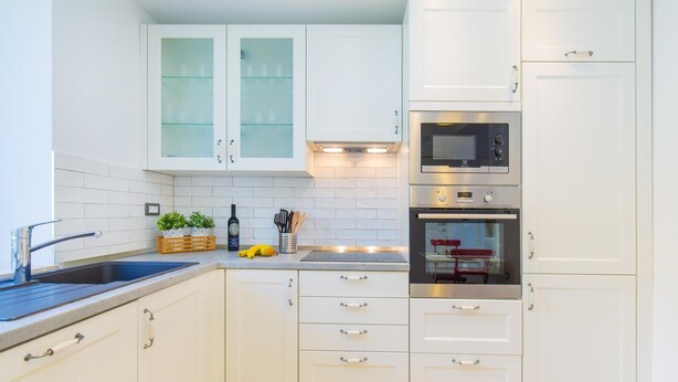 Eine moderne Küche mit weißen Schränken, einer doppelten Spüle und Edelstahlgeräten, darunter eine Mikrowelle und ein Backofen.