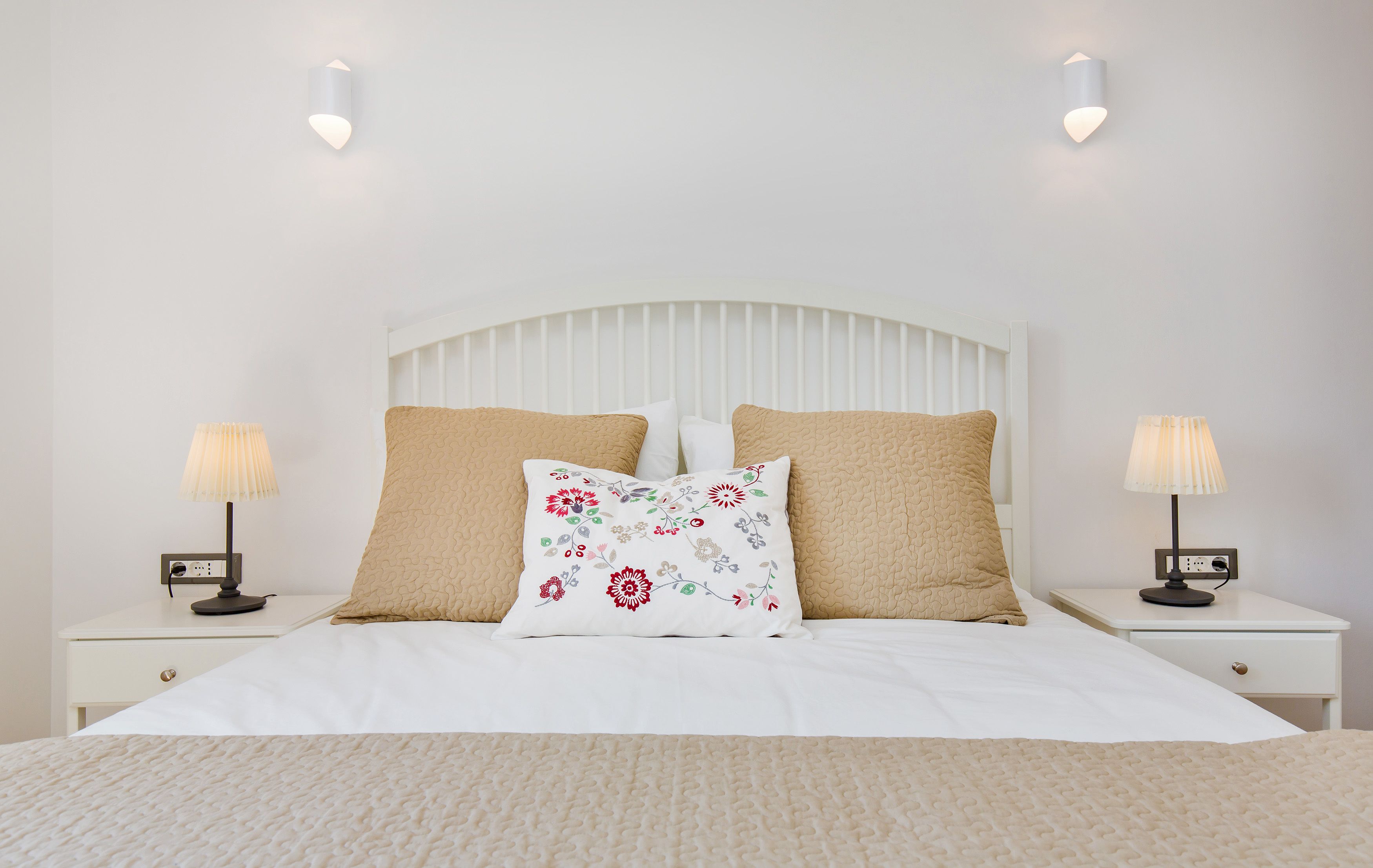 Un lit bien fait, avec une tête de lit blanche, deux lampes de chevet et un coussin à motifs floraux.
