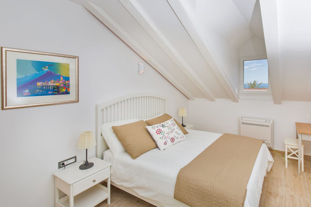 A bedroom with a bed, bedside table, lamp, and a painting on the wall.