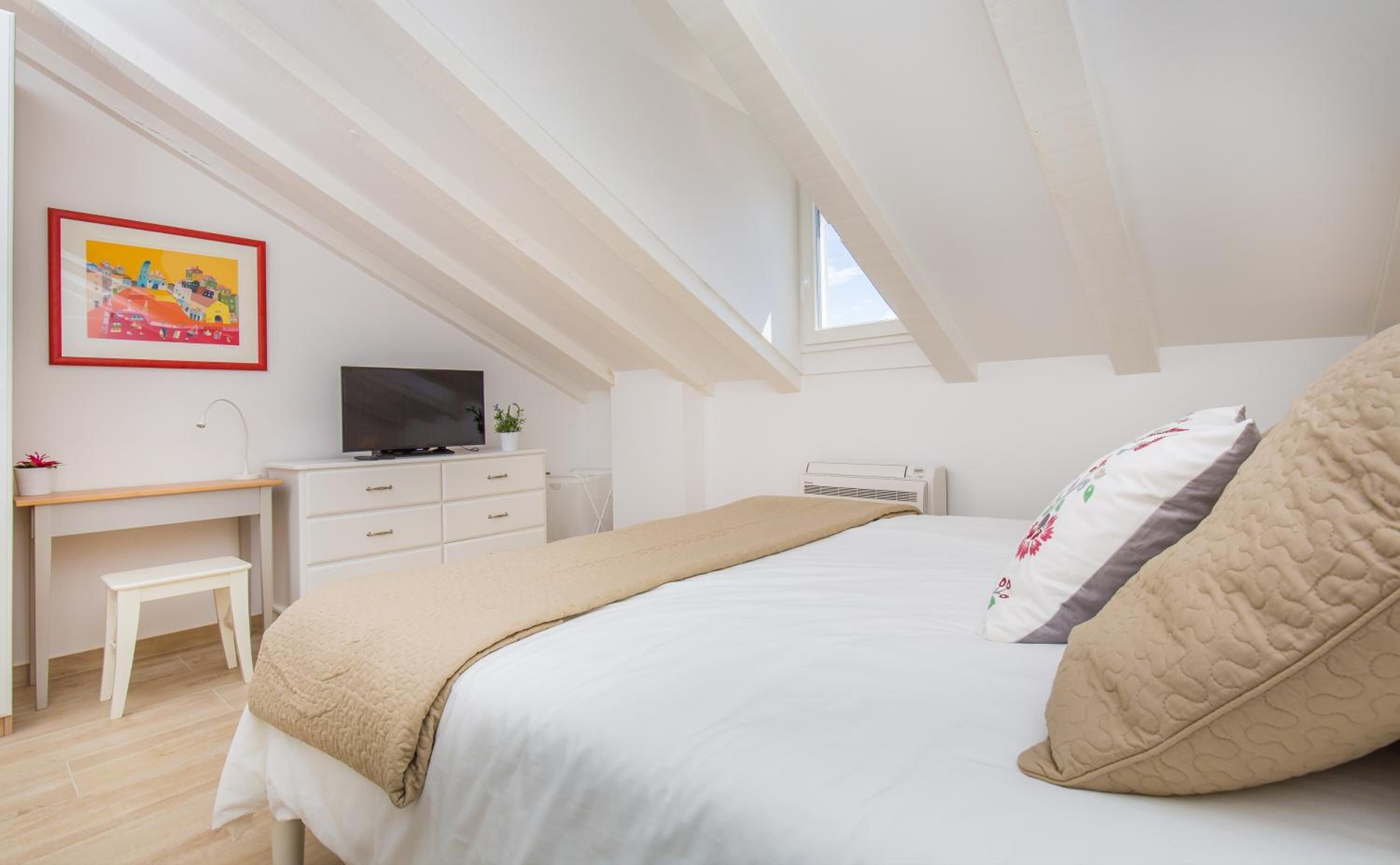 A bedroom with a bed, a desk, a TV, and a window.