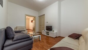 A modern living room with a grey sofa, a beige sofa, a glass coffee table, a flat-screen TV on a white stand, and a wooden floor.