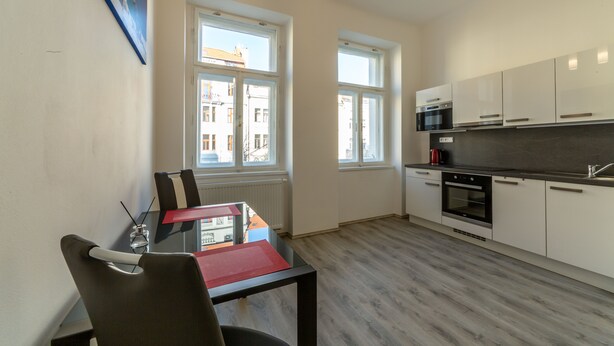 A modern kitchen with white cabinets, a black countertop, and two ovens. There is a dining table with chairs and a red placemat.