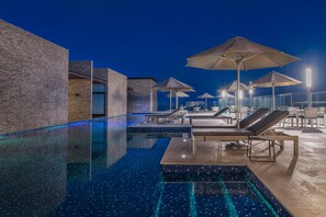 A nighttime swimming pool area with lounge chairs and umbrellas, surrounded by a modern building with a brick facade. - Trendy 1BR Apartment in Cruz con Mar brand new building by Happy Address (Playa del Carmen)