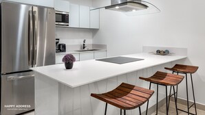 A modern kitchen with a stainless steel refrigerator, a microwave, and a sink. There are three wooden stools at the island. - Trendy 1BR Apartment in Cruz con Mar brand new building by Happy Address (Playa del Carmen)