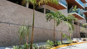A modern building with multiple balconies, a landscaped area with palm trees, and a paved walkway. - Full Stylish 2BR apartment in heart of town by Happy Address (Playa del Carmen)