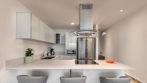 A modern kitchen with a central island, stainless steel appliances, and three bar stools. - New and modern 2BR downtown apartment by Happy Address (Playa del Carmen)