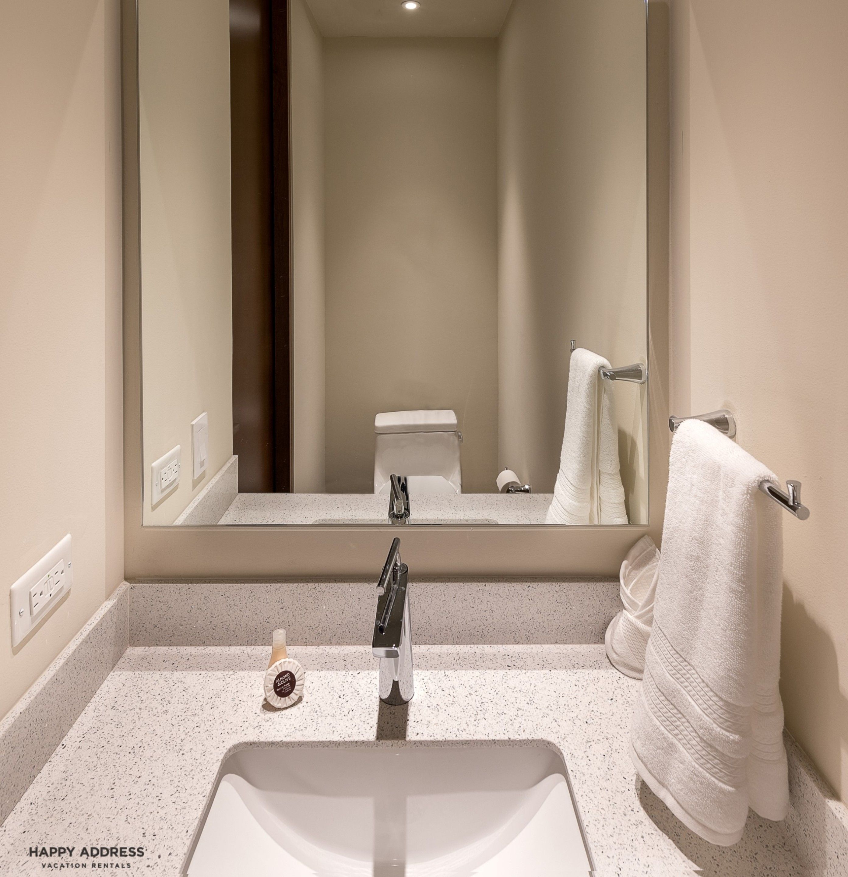 Ein Badezimmer mit einem weißen Waschbecken, einem Spiegel, einem Handtuchhalter und einer Toilette.