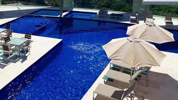 A swimming pool with lounge chairs and umbrellas, surrounded by a clear view of the ocean. - Pleasant 1BR a few step away from the beach by Happy Address (Playa del Carmen)