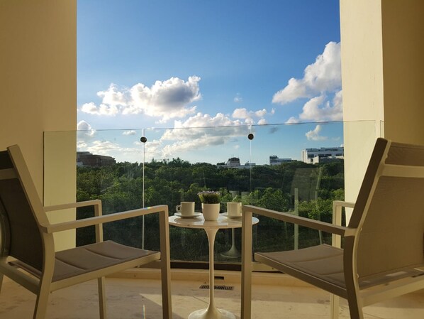 A balcony with two chairs and a small table, overlooking a cityscape with greenery and buildings. - Brand New 1 BR Condo with jungle view by Happy Address (Playa del Carmen)