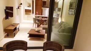 A modern living room with a glass door leading to a dining area. There are two wicker chairs with white cushions, a small round table, and a sofa visible through the glass. - Cozy 1 BR apartment steps away from the Beach by Happy Address (Playa del Carmen)