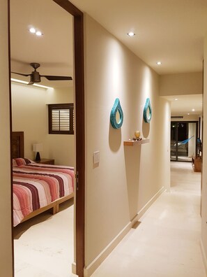 A hotel hallway with a bed, ceiling fan, and decorative wall art. - Caribbean Lifestyle 2BR steps from the beach by Happy Address (Playa del Carmen)