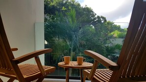 A wooden chair and table set on a balcony with a view of lush greenery. - Caribbean Lifestyle 2BR steps from the beach by Happy Address (Playa del Carmen)