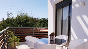Un balcone con un tavolo rotondo e quattro sedie bianche, una pianta in vaso e un'ampia finestra.