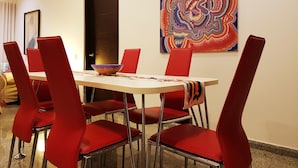 Zona pranzo con tavolo, sedie rosse, una ciotola e un quadro astratto colorato appeso al muro.