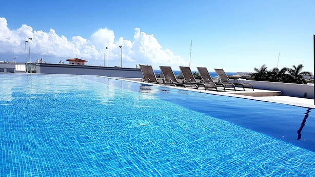Una piscina blu cristallina con lettini lungo il bordo, cielo sereno e un edificio in lontananza.