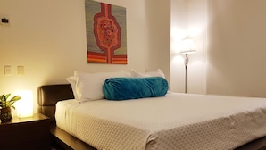 Un letto rifatto con un cuscino bianco e blu, un elemento decorativo a parete e una lampada da terra.
