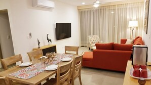 A modern living room with a red sofa, a wooden dining table set with plates and glasses, and a TV mounted on the wall. - Cute 1 BR in amazing location by Happy Address (Playa del Carmen)