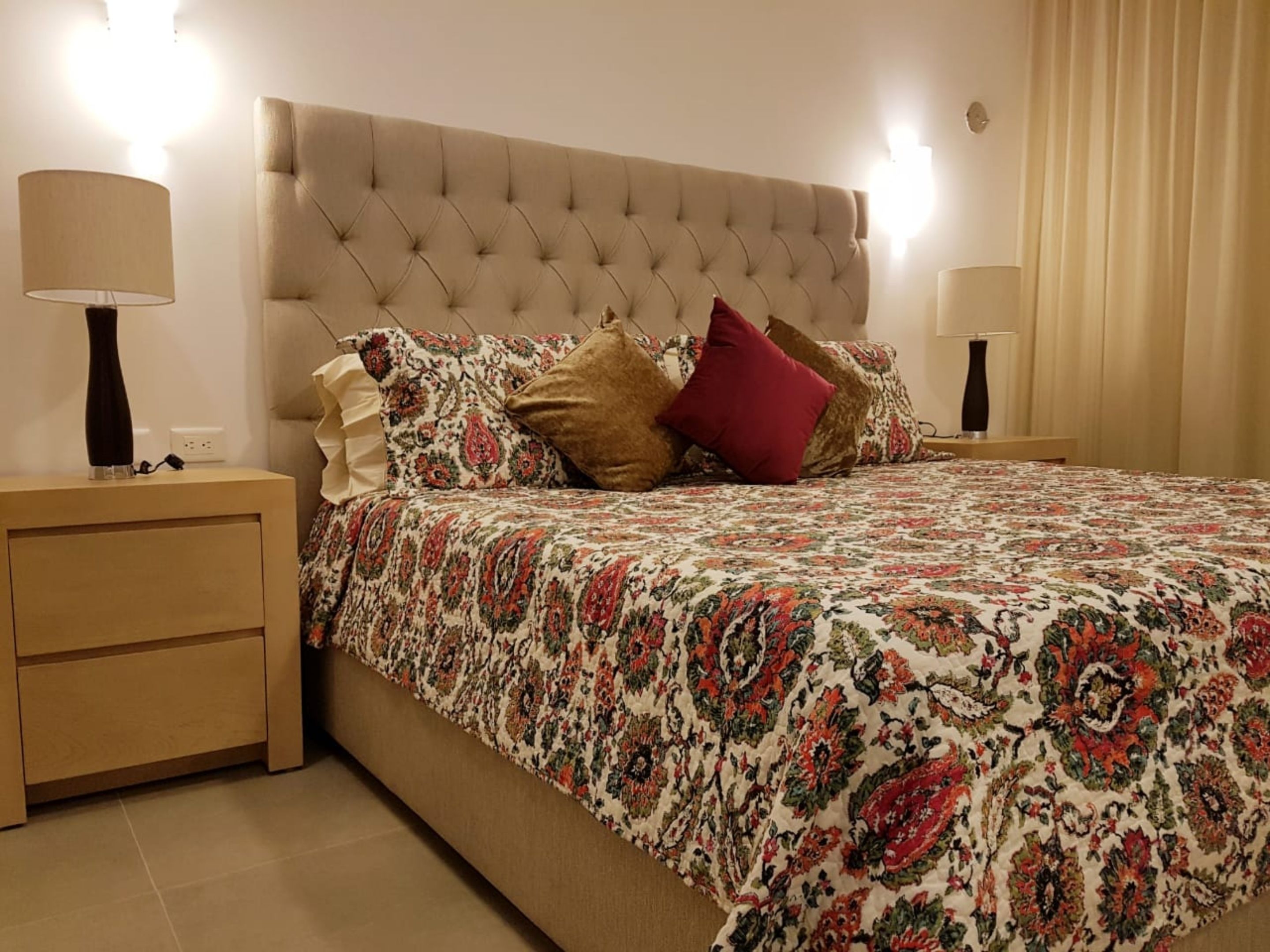 A neatly made bed with a patterned bedspread, two bedside tables with lamps, and a wall-mounted light fixture.