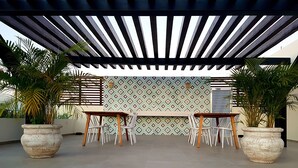 An outdoor patio with a pergola, two wooden tables, and potted plants. - Cute 1 BR in amazing location by Happy Address (Playa del Carmen)