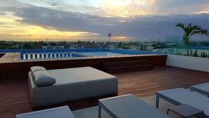 A rooftop terrace with a pool, lounge chairs, and a view of the city skyline at sunset. - Cute 1 BR in amazing location by Happy Address (Playa del Carmen)