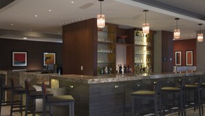 Uma área de bar moderna com bancada de granito, banquetas e iluminação pendente.