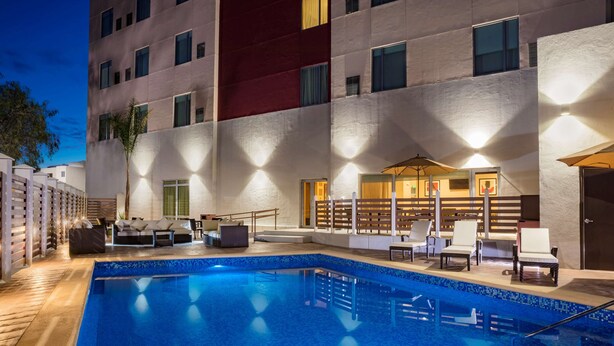 Piscina com espreguiçadeiras e guarda-sóis, cercada por um edifício com vários andares e varandas.