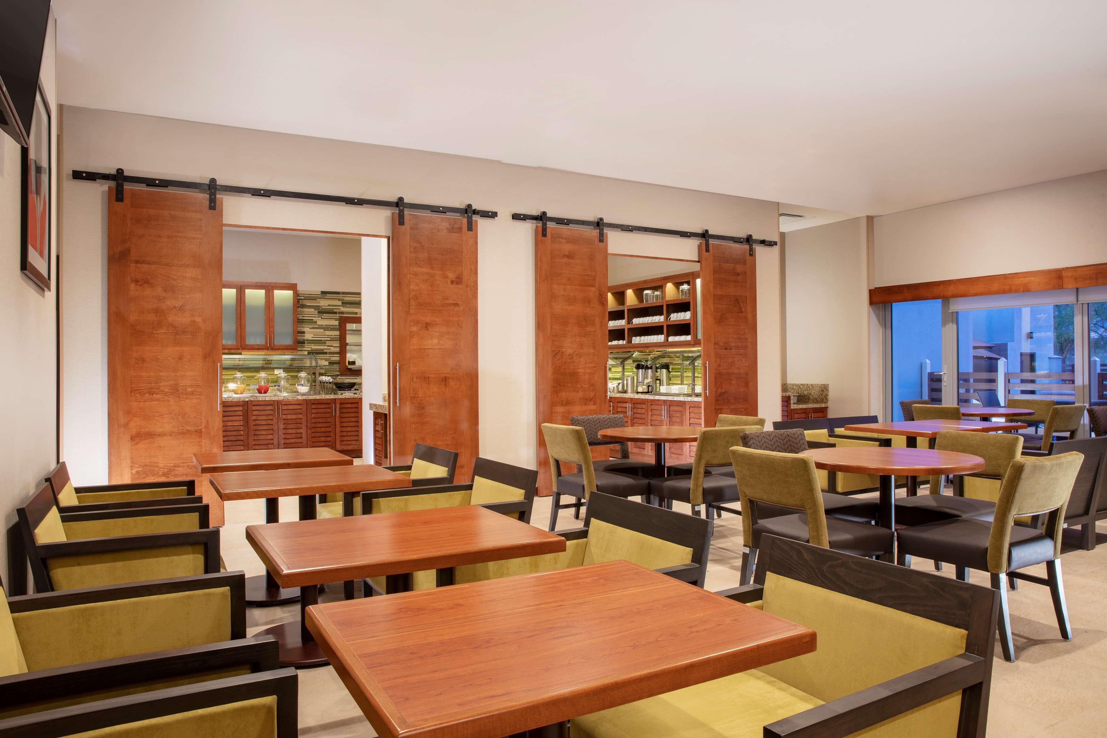 Un restaurante con mesas y sillas de madera, una zona de cocina y vistas amplias a través de grandes ventanales.