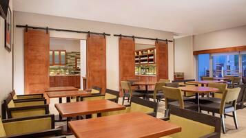 Un restaurante con mesas y sillas de madera, una zona de cocina y vistas amplias a través de grandes ventanales.