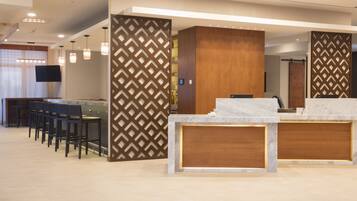 Un área de recepción moderna con mostrador de mármol, paneles de madera y zona de estar con sillas.