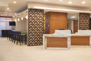 A modern reception area with a marble counter, wooden paneling, and a seating area with chairs.