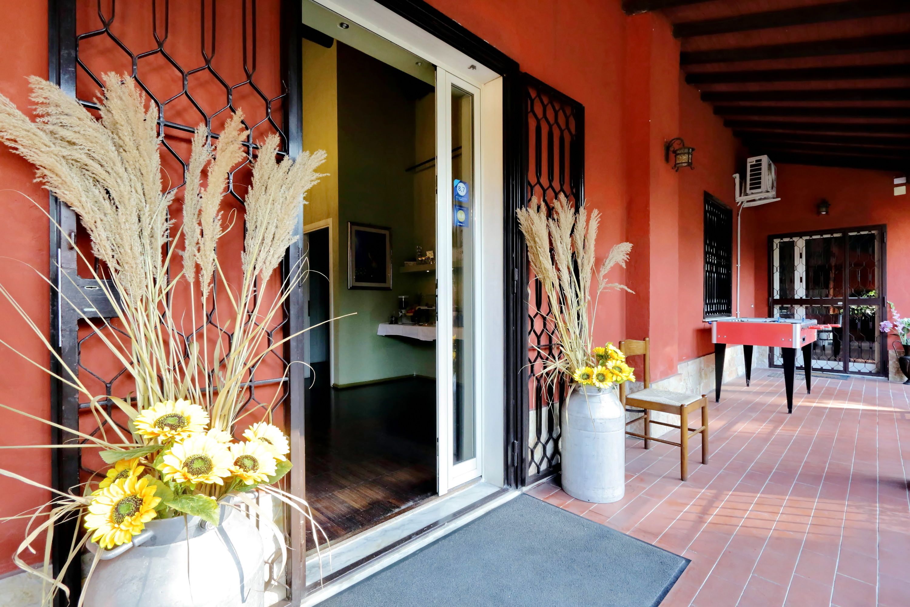 A hotel entrance with a red exterior, a glass door, and a patio area with a table and chairs.