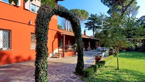 Un patio con un sendero de piedra, un área de descanso cubierta y un edificio con paredes anaranjadas.