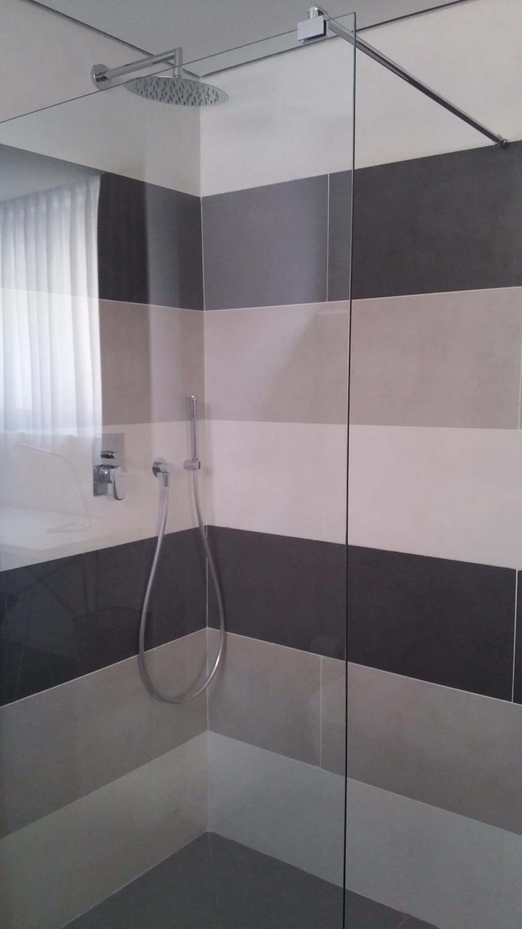 A modern bathroom with a glass shower enclosure, a visible showerhead, and a tiled wall with a striped pattern.