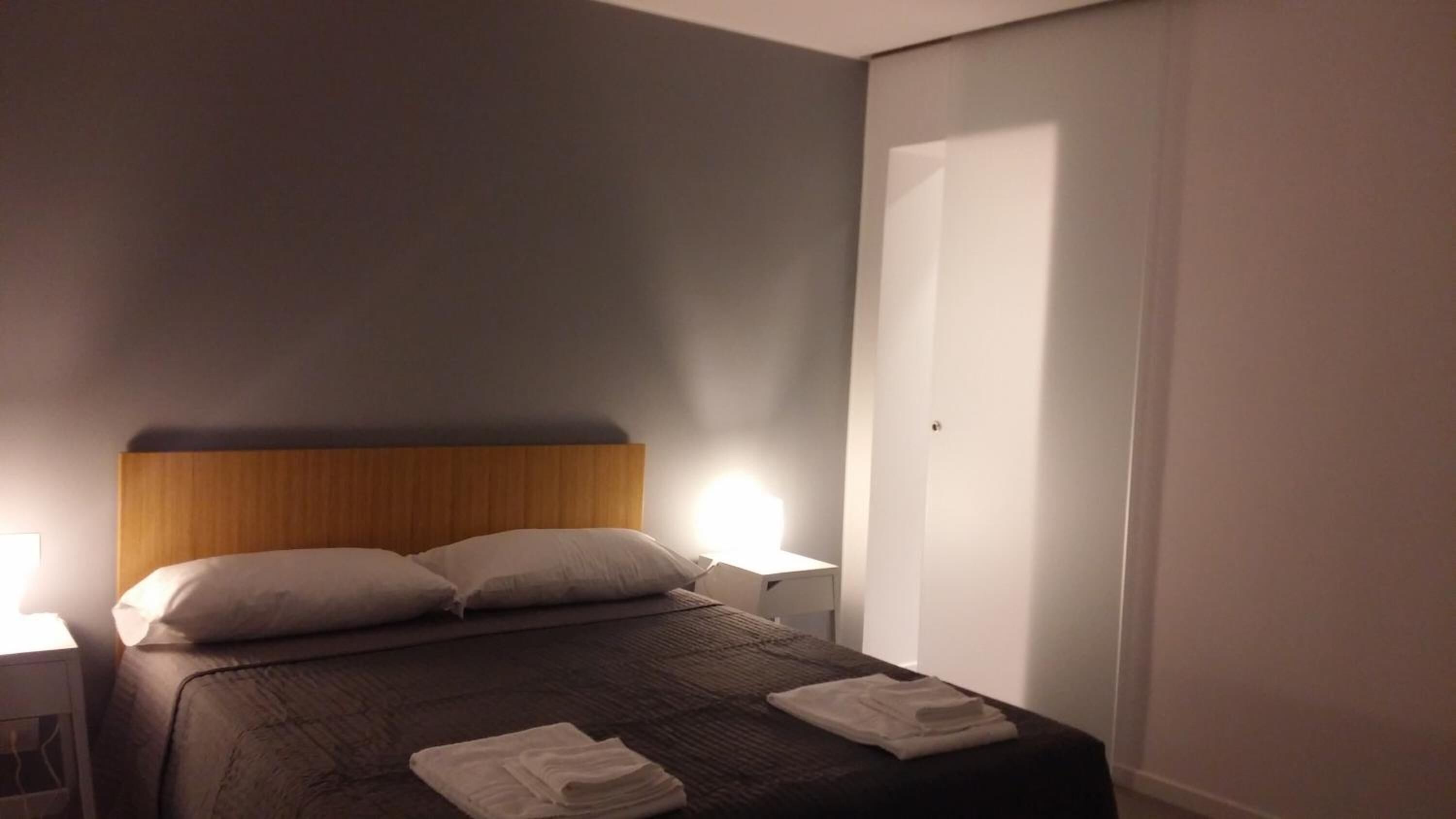 A neatly made bed with a wooden headboard, two bedside lamps, and a folded towel on the bed.