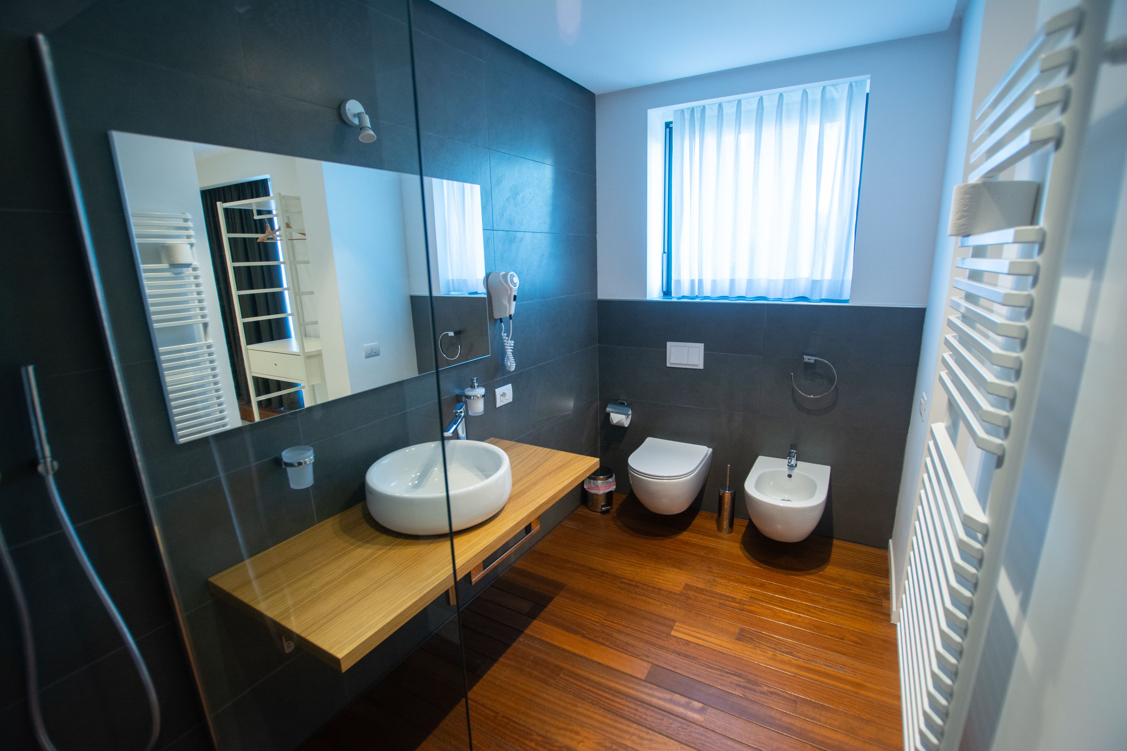 Ein modernes Badezimmer mit einem Holzbadezimmermöbel, einem großen Spiegel, einem Bidet und einem Fenster mit Vorhängen.