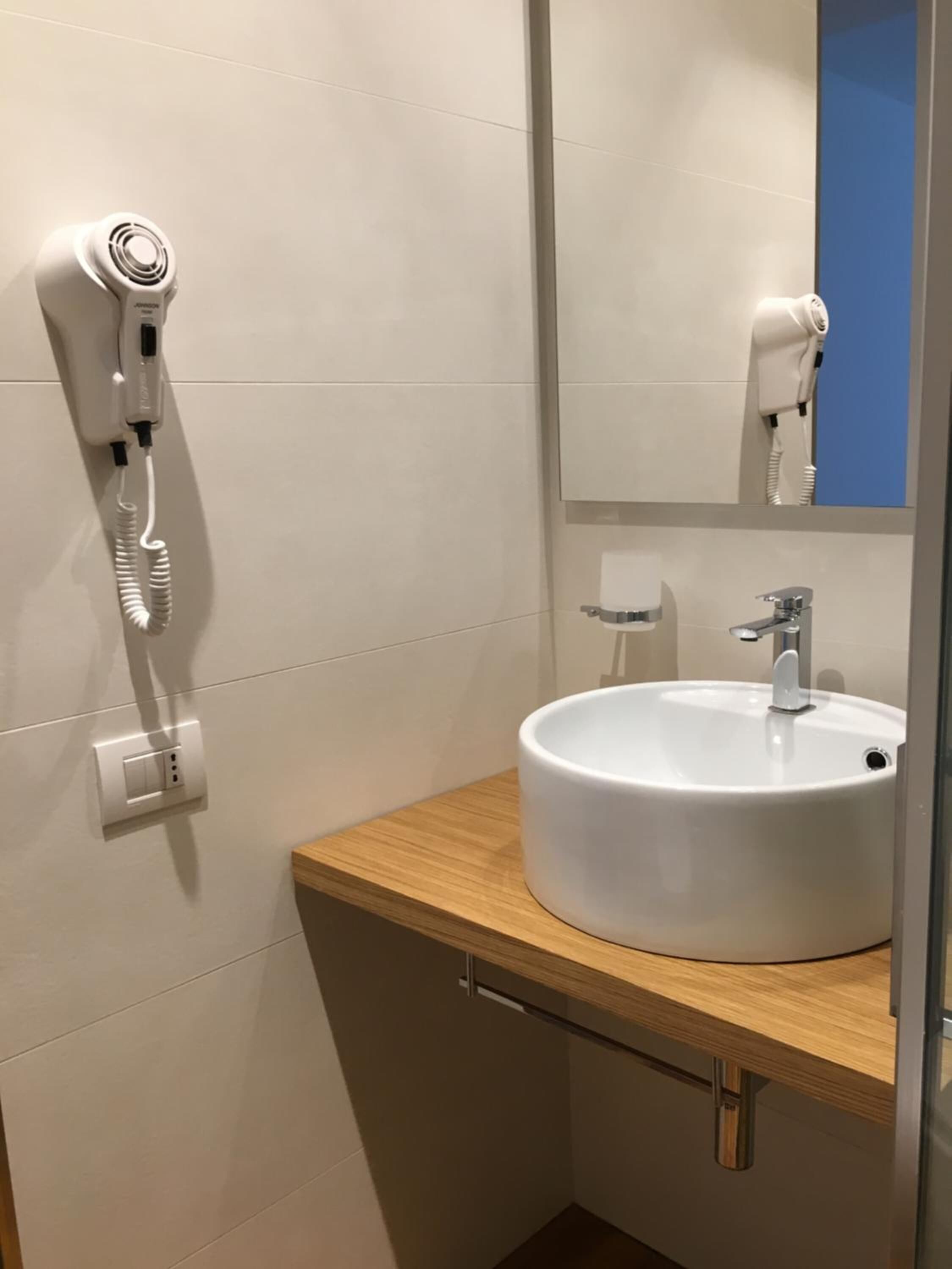 A bathroom with a white sink, a mirror, and a hairdryer mounted on the wall.