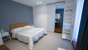 A modern bedroom with a bed, bedside tables, a walk-in closet, and a bathroom visible through an open door. - B&B Brezza di Mare (Aci Castello)