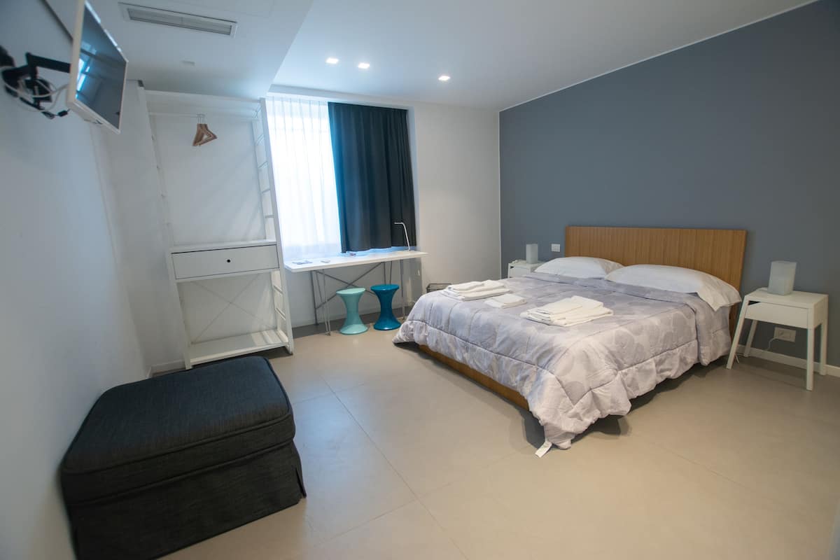 Une chambre d’hôtel moderne équipée d’un lit, d’un bureau, d’une chaise et d’un téléviseur fixé au mur.