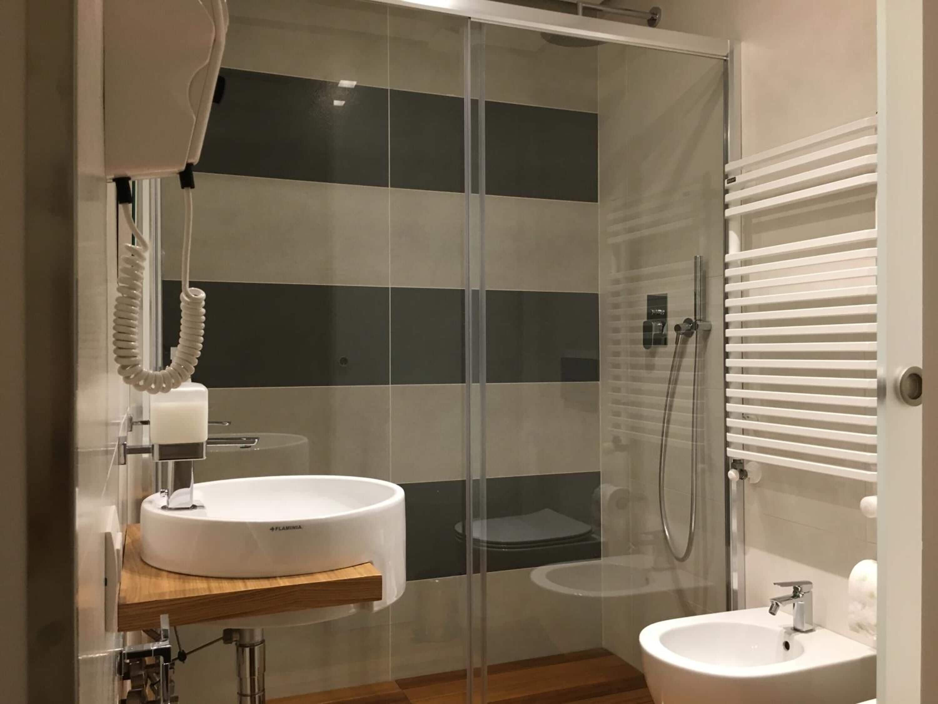 Une salle de bain moderne dotée d’une douche à parois de verre, d’un meuble-lavabo en bois et d’un espace lavabo séparé.