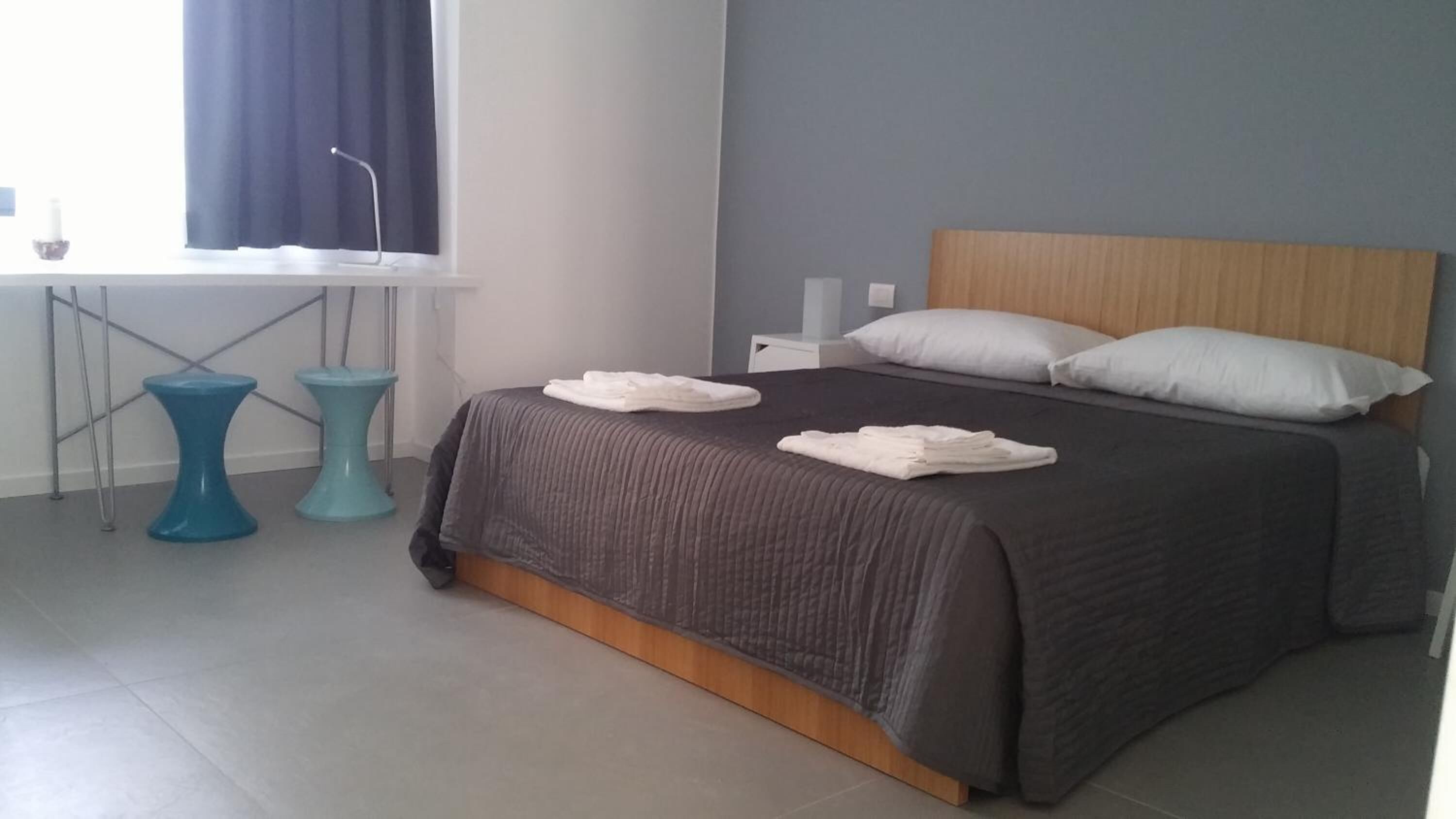 Quarto moderno com uma cama grande, cabeceira de madeira e janela com cortinas.