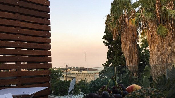 A balcony with a table and chairs, a bowl of fruit, and a view of a cityscape. - B&B Brezza di Mare (Aci Castello)