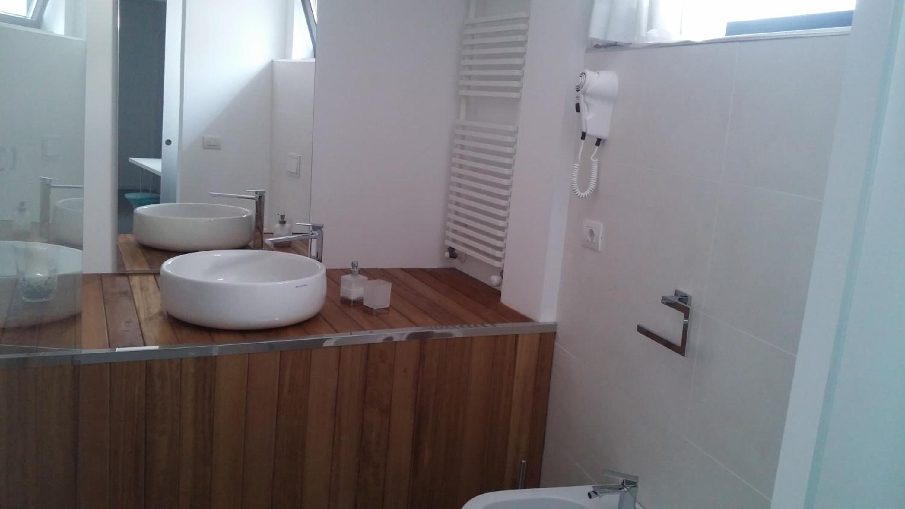 Een badkamer met twee ronde wasbakken, een houten wastafelmeubel, een spiegel, een toilet en een haardroger aan de muur.