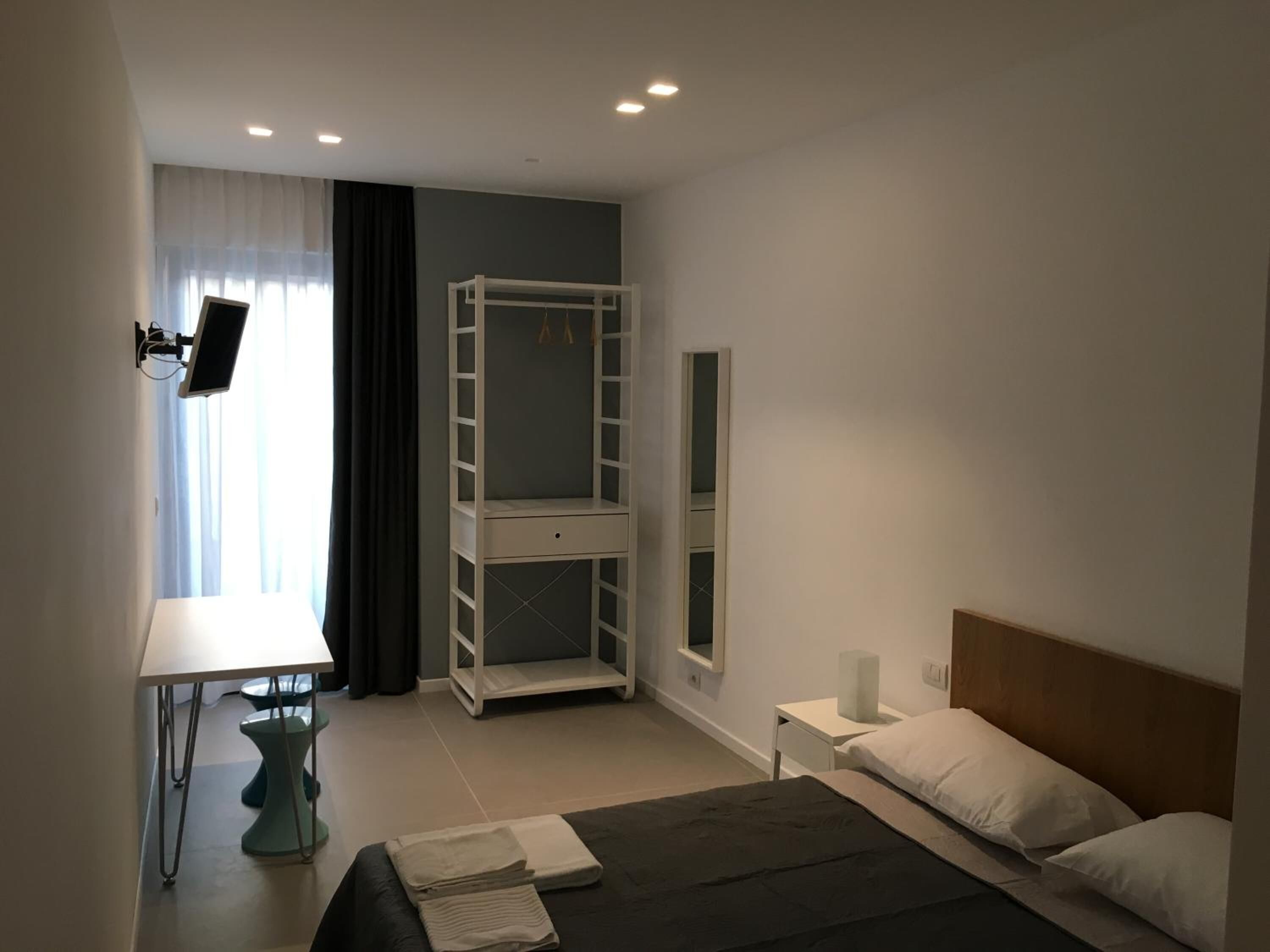 A bedroom with a bunk bed, a desk with a computer, a chair, and a bedside table with a lamp.